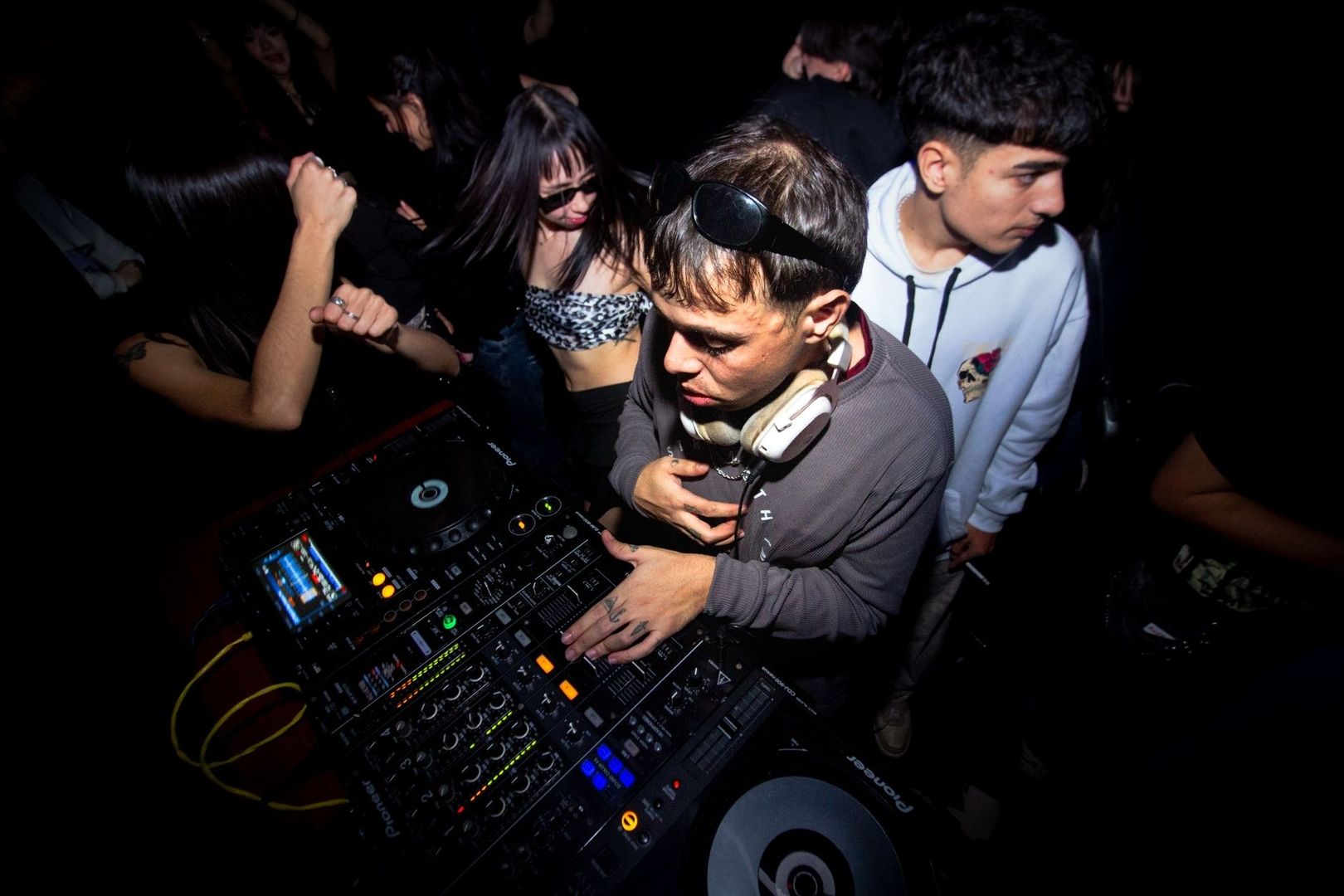 DJ mixar musik medan människor dansar tätt intill i ett mörkt rum